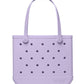 The Baby Bogg® Bag by Bogg Bags is a light purple, rectangular tote featuring two handles and a distinctive pattern of small round holes on the front. This washable bag has “bogg” embossed on the lower right corner, offering both practicality and style.