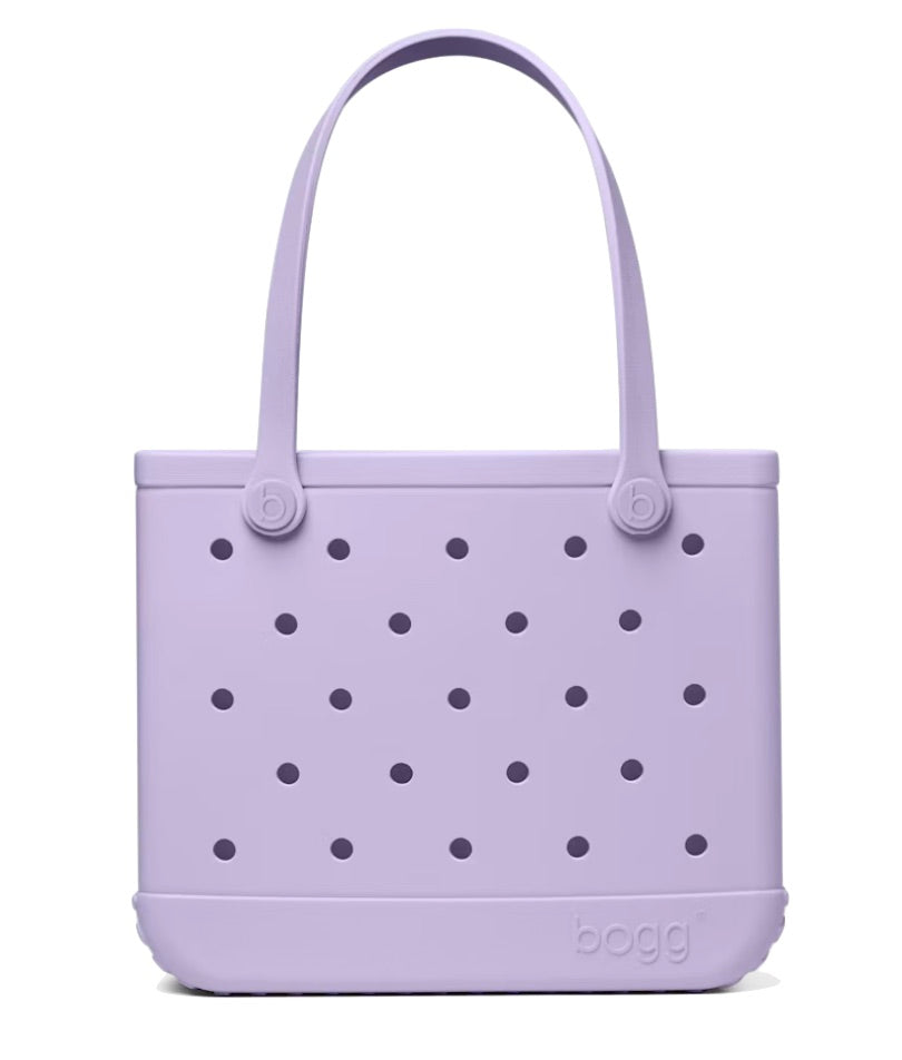 The Baby Bogg® Bag by Bogg Bags is a light purple, rectangular tote featuring two handles and a distinctive pattern of small round holes on the front. This washable bag has “bogg” embossed on the lower right corner, offering both practicality and style.
