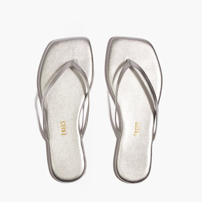 The Tkees Lily Square Toe Metallic Sandal features thin straps and a modern square-toe design in metallic silver, shown on a white background.