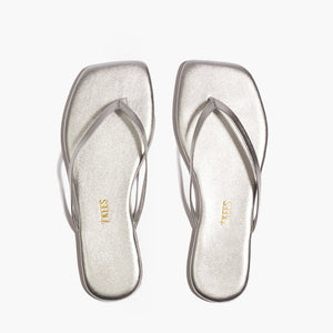 The Tkees Lily Square Toe Metallic Sandal features thin straps and a modern square-toe design in metallic silver, shown on a white background.