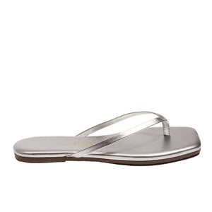 The Tkees Lily Square Toe Metallic Sandal is a silver flat flip-flop with clean lines, a slim toe strap, and a brown sole, shown from the side.