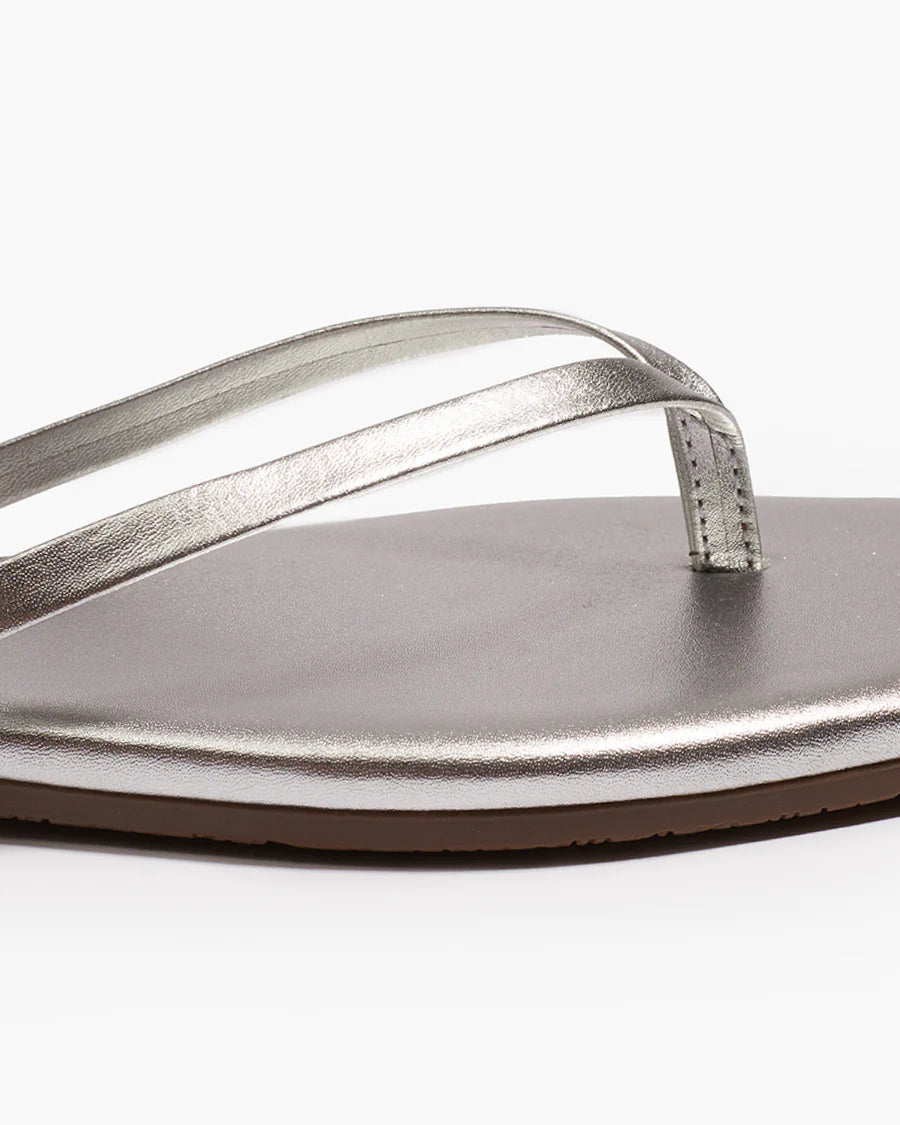 Close-up of the Tkees Lily Square Toe Metallic Sandal, featuring thin straps and a flat sole in metallic silver, displaying clean lines and modern design against a white background.