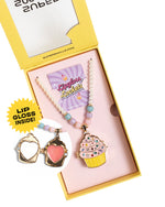 An open yellow box displays the Super Smalls Cupcake Lipgloss Locket kids necklace, with beads and a "Lipgloss Locket" card. An inset shows the locket open, revealing pink lip gloss inside. Text reads "LIP GLOSS INSIDE!.