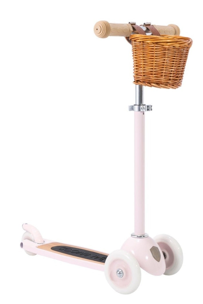 A pink child's Banwood Scooter with a wicker basket attached to the handlebars, featuring an Easy Ride Steering System.