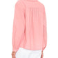 Woman wearing the Xirena Dany Shirt, an airy blouse with lace inset detailing, and white pants, shown from the back with her head turned slightly to the side.