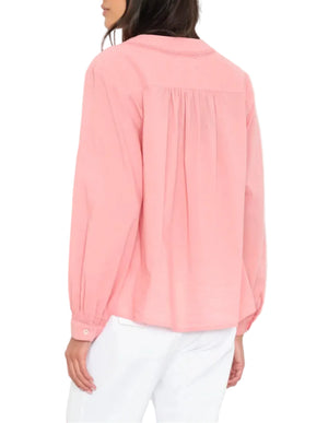 Woman wearing the Xirena Dany Shirt, an airy blouse with lace inset detailing, and white pants, shown from the back with her head turned slightly to the side.