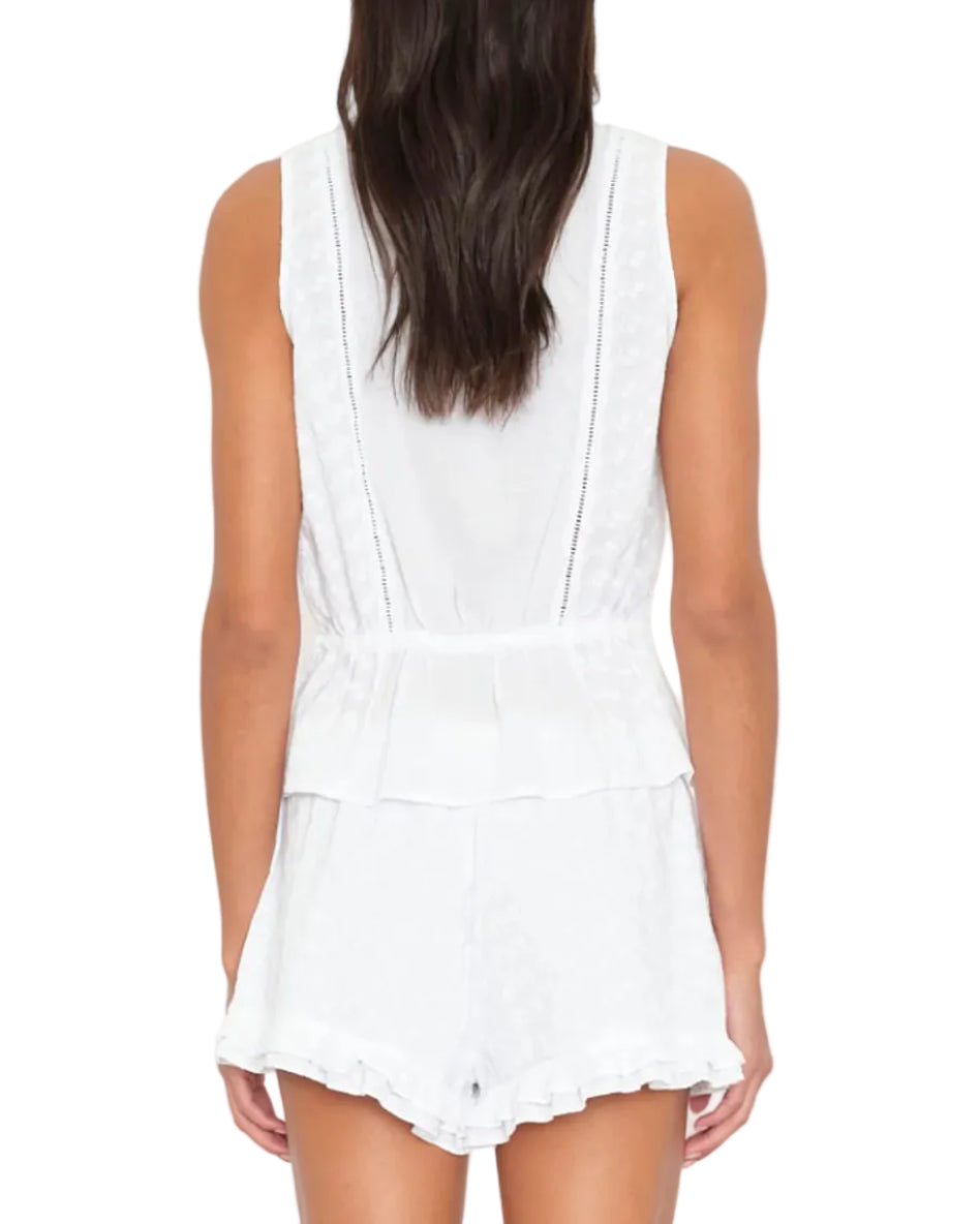 A woman is shown from the back wearing the sleeveless white Emma Top by Xirena, featuring a peplum waist and delicate lace inset details.
