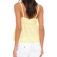A woman faces away in the Xirena Alexia Top—a yellow camisole with thin straps—paired with white cotton poplin pants, set against a plain white background.