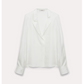 The Dorothee Schumacher Trench It Up Blouse is a white silk twill top with long sleeves, an asymmetric notched lapel, and wide cuffs, shown on a light background. Its fluid drape highlights the elegant silhouette.