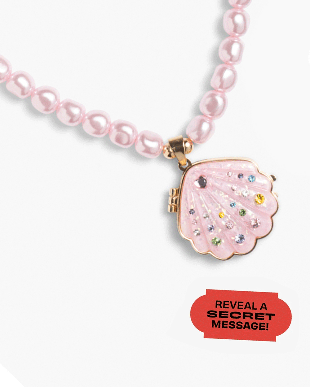 The Super Smalls Sparkle Shell Lipgloss Locket is a pink beaded necklace featuring a seashell-shaped jeweled locket. A red label reads, "REVEAL A SECRET MESSAGE!.