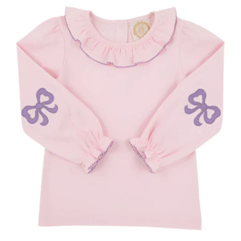 The Girls' Long Sleeve Ramona Ruffle Shirt by The Beaufort Bonnet Company features a light pink design with a ruffled collar, purple trim, and sweet bow accents—ideal for a stylish back-to-school outfit.