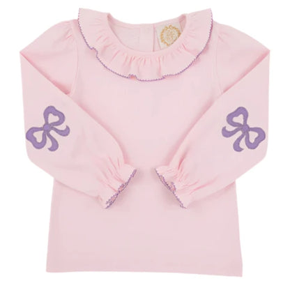 The Girls' Long Sleeve Ramona Ruffle Shirt by The Beaufort Bonnet Company features a light pink design with a ruffled collar, purple trim, and sweet bow accents—ideal for a stylish back-to-school outfit.
