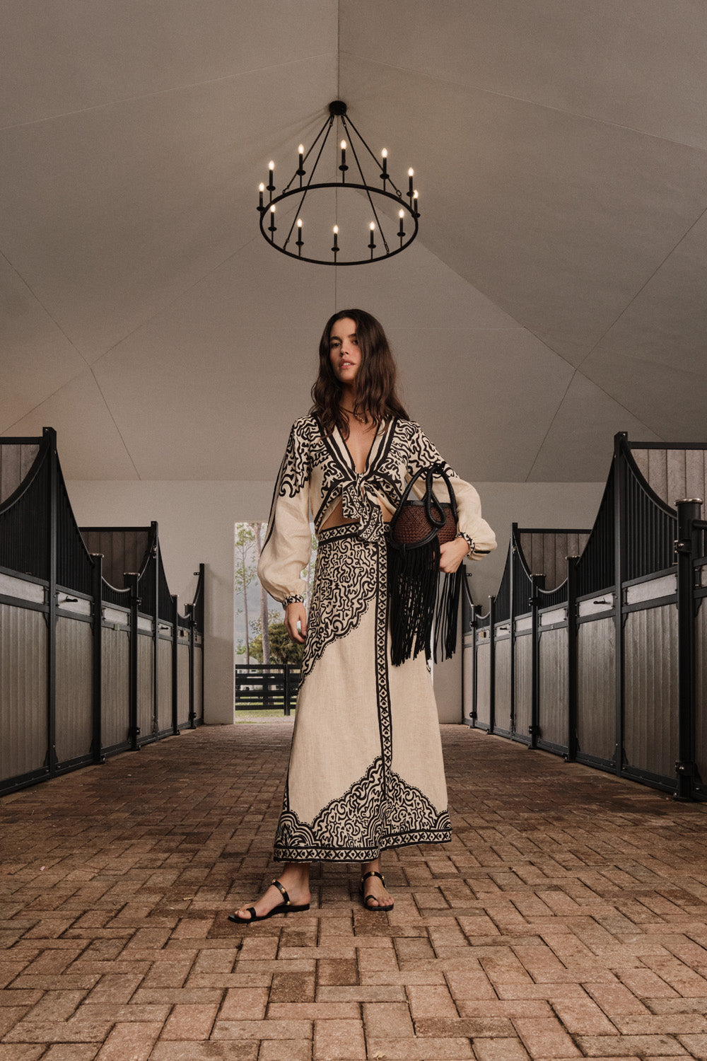 A woman wears a black and white geometric print Loose Horizon Ankle Skirt with an embroidered border, carrying a black fringed handbag.