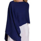 A woman stands against a white background, wearing the Alashan Cashmere Cashmere Dress Topper Poncho in loose navy blue layered over white pants—a versatile choice for effortless day-to-night style.