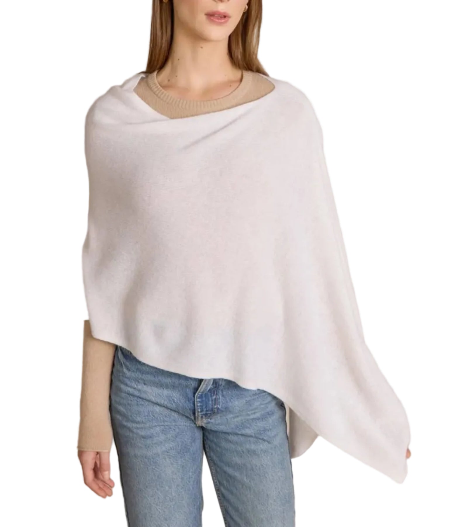 A woman wearing a beige sweater, light blue jeans, and the Alashan Cashmere Dress Topper Poncho in white stands against a white background, effortlessly exemplifying the versatile elegance of this staple piece—perfect for transitioning seamlessly from day to night.