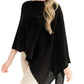 A woman with loose wavy hair stands against a white background, wearing the Alashan Cashmere Cashmere Dress Topper Poncho in black, styled as a versatile wardrobe staple over light-colored pants.