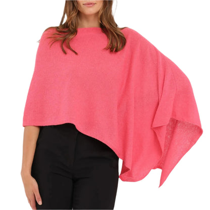 A woman exudes effortless style in the vibrant pink Cashmere Dress Topper Poncho by Alashan Cashmere, the ideal wardrobe essential for a seamless day-to-night transition, elegantly draped over black pants.