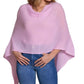 A woman models the Alashan Cashmere Cashmere Dress Topper Poncho in light pink—an effortless wardrobe essential—paired with blue jeans and her hands resting on her hips.