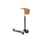 The Banwood Scooter is a vintage-style black three-wheeled kick scooter with a tan handlebar and front woven basket, designed to help kids develop coordination while riding in style.