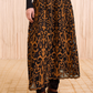 Person wearing a black long-sleeve top, Ulla Johnson's Gili Midi Skirt with brown and black patterns, black leggings, and black pointed-toe ankle boots on a patterned floor.