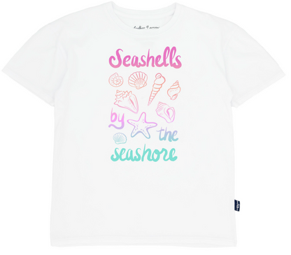 The Feather 4 Arrow Girls’ Oversized Tee is made from premium cotton and features pastel illustrations of seashells along with the phrase “Seashells by the seashore” in pink, purple, and teal.