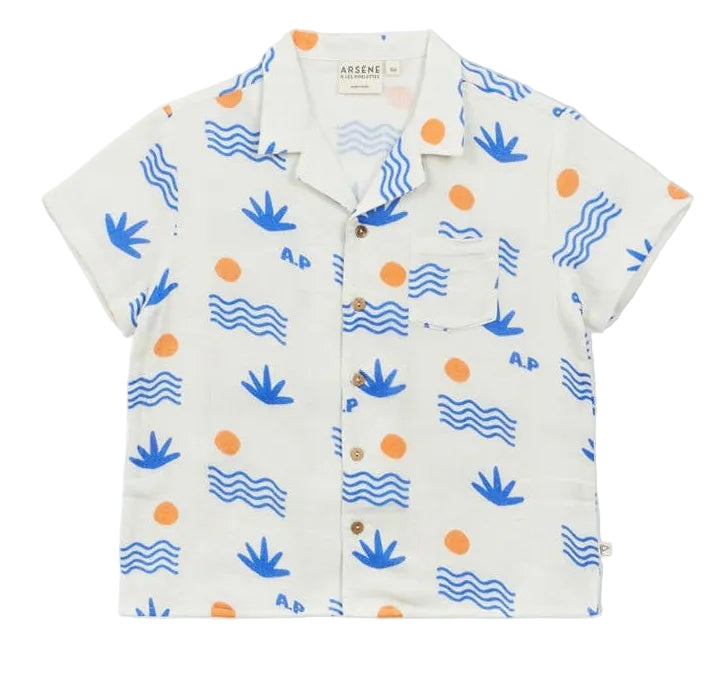 The Arsene & Les Pipelettes Boys' Magnum Shirt is a short-sleeve white double voile shirt featuring blue wave and plant motifs, orange sun accents, a chest pocket, and brown buttons, showcased against a plain background.