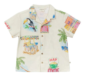 The Boys' Magnum Shirt by Arsene & Les Pipelettes is a short-sleeve, button-up cotton shirt featuring vibrant prints of toucans, palm trees, fruit stands, and playful "HAY" and "COCOS" signs on a light background. It’s designed in a relaxed fit to keep boys comfortable all day long.