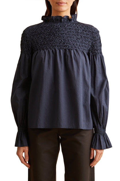 The model is wearing a Merlette New York Merlette Majorelle Top with ruffled sleeves.