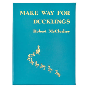 Cover of Graphic Image's "Make Way For Ducklings, Leather" by Robert McCloskey, featuring gold illustrations of Mallards leading ducklings on a teal background that bring the illustrated tale to life.