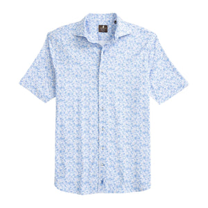 The Johnnie-O Filipe Shirt is a coastal-inspired short-sleeve button-up featuring a light blue floral pattern on a white background, complete with a smart button-down collar and shown laid flat on a white surface.