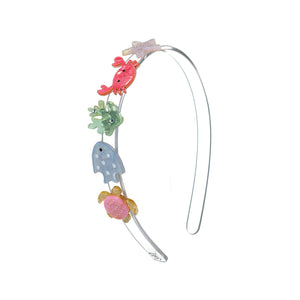 The Lillies & Roses Ocean Friends Crab Headband is a handmade silver accessory adorned with colorful, glittery charms—including a crab, fish, turtle, seaweed, and jellyfish—making it a playful statement piece shown here on a white background.