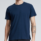 A person wearing the Rag & Bone Classic Flame Tee, a plain navy blue short-sleeve T-shirt crafted from durable Peruvian cotton, along with black pants and displaying tattoos on both forearms, is standing against a neutral background.