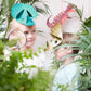 Two children wearing dinosaur masks stand among leafy plants, ready for a prehistoric party. One holds a magnifying glass, while Meri Meri's charming dinosaur decoration and playful Meri Meri Party Hats complete the adventurous scene in the background.