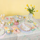 An Easter table setting bursts with ideas, featuring a bunny plate, eggs, cupcakes, and tulips on a Meri Meri Easter Colour In Activity Tablecloth that creatively adds color to your festive feast.