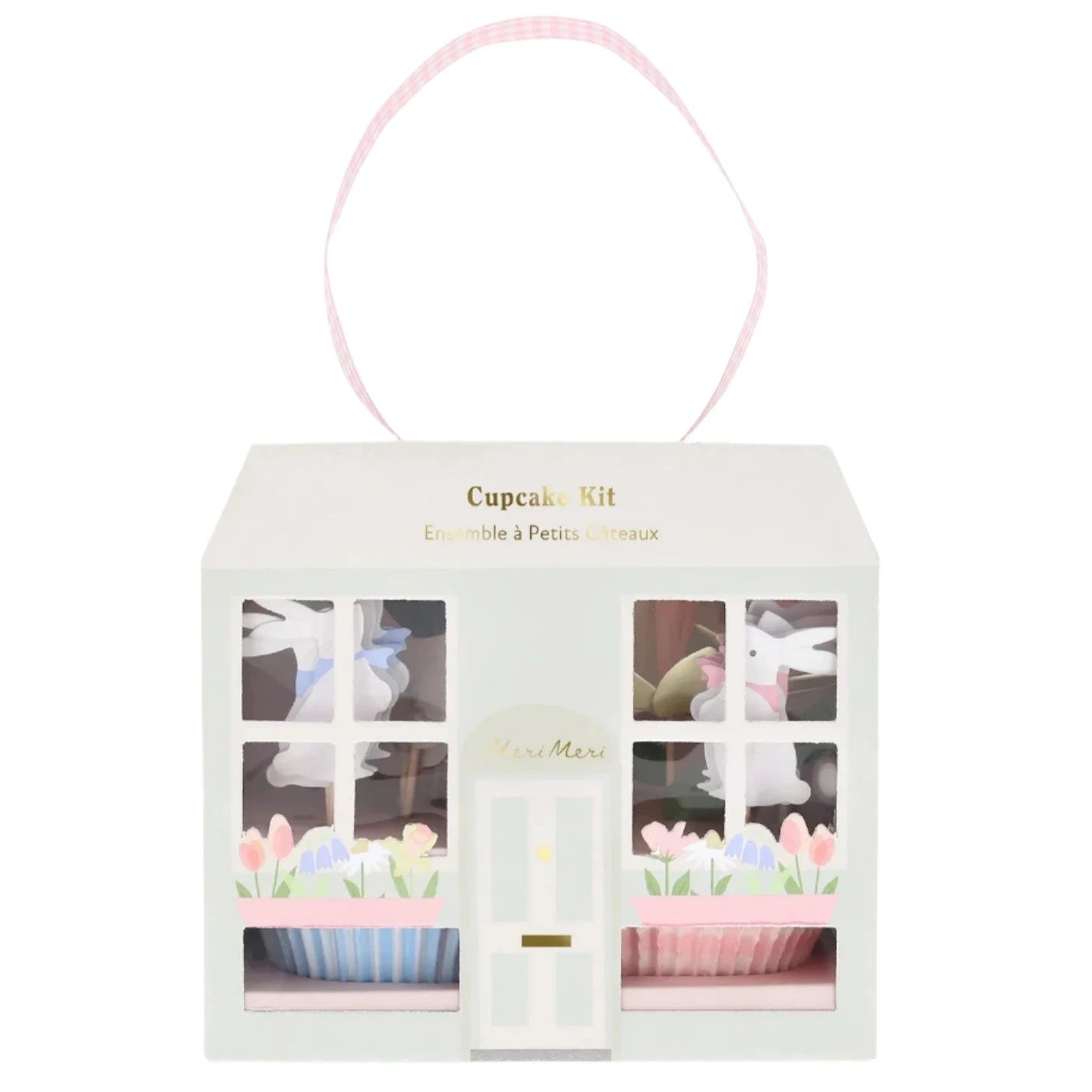 The Meri Meri Easter Cottage Cupcake Kit showcases a pastel storefront design with window cutouts revealing decorative bunnies and flowers, complemented by a pink checkered handle on top, perfect for inspiring creative baking with springtime toppers.