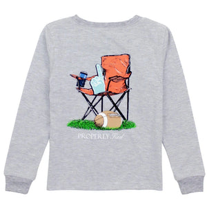 The Properly Tied Boys' Long Sleeved Tee is a gray shirt with hand-drawn graphics of an orange folding chair holding a foam finger and drink next to a football on grass, with "PROPERLY Tied" text below.