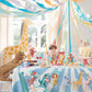 A child sits at a table decorated for a party with an animal theme. Streamers hang from the ceiling, and stuffed animal toys, Meri Meri Party Cups, and vibrant decorations adorn the room.