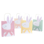 Four vibrant Easter Party Bags by Meri Meri, featuring rabbit designs and 3D bows in pink, yellow, green, and blue, are lined up perfectly for an Easter egg hunt.