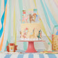 A beautifully decorated cake with Meri Meri Cake Toppers is displayed on a pink stand, surrounded by colorful streamers and animal-themed party items.