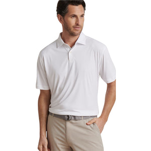 A man wears a Peter Millar Featherweight Mélange Polo with UPF 50+ sun protection, tucked into light beige pants and styled with a grey belt, standing with one hand in his pocket.