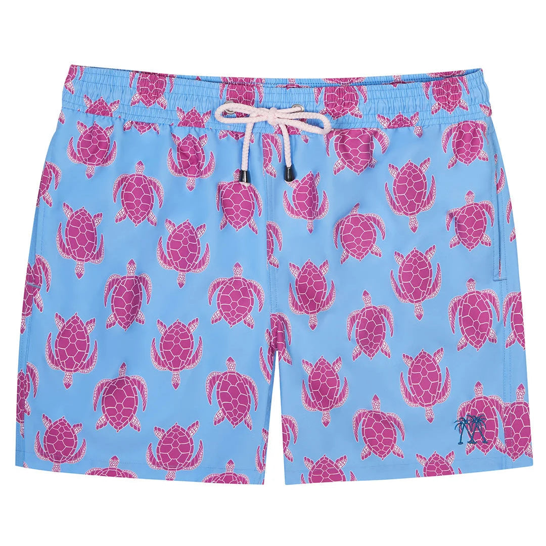 The Pink House Mustique Turtle Trunks are light blue quick-dry swim shorts featuring a playful pink sea turtle pattern, white drawstring, and a comfortable elastic waistband.