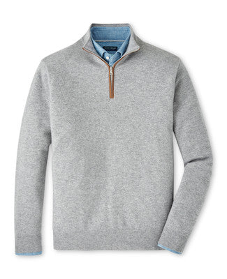 The Peter Millar Artisan Crafted Cashmere Flex Quarter-Zip in light gray features a brown zipper pull and classic British knitwear inspiration, layered over a blue collared shirt and shown on a white background.