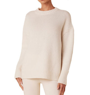 A person wearing a cream-colored, long-sleeved, cozy Sablyn Mimi Crewneck Sweater with ribbed cuffs and a ribbed neckline and hem, and matching cream pants.