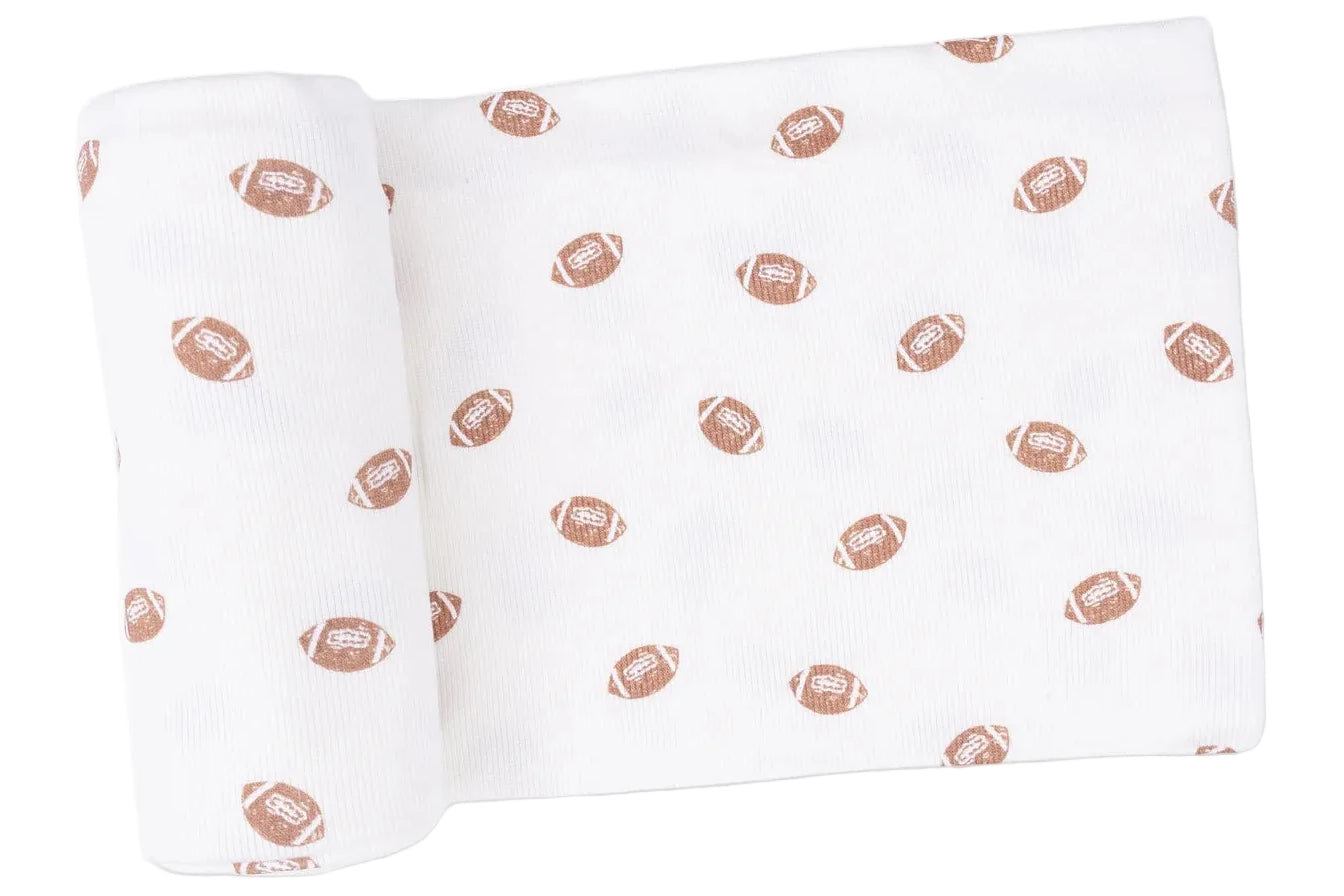White fabric rolled at one end, patterned with small brown footballs evenly spaced across the surface—this Angel Dear Swaddle Blanket is crafted from soft Viscose from Bamboo for ultimate comfort.