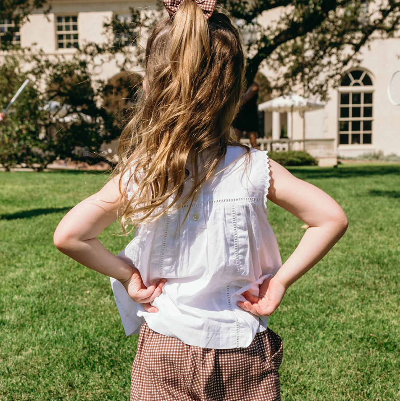 A girl wearing the Minnow Girls' White Align Tank stands in a grass field, enjoying the fresh air.