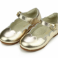 The Girls' Sonia Scalloped Flat by L'Amour Shoes features gold metallic finish, scalloped trim, ankle straps, and small buckles—an essential flat for girls shown on a white background.