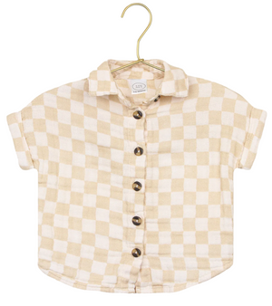 The Lou Lou & Company Baby Boys’ Cloud Muslin Shirt, featuring a beige and white checkered design with short sleeves and button-up front, hangs on a gold hanger against a white background—a versatile piece with a relaxed fit, ideal for casual days.