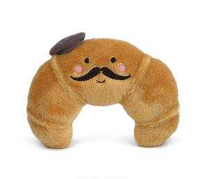 Monsieur Croissant by Mon Ami is a plush toy featuring embroidered eyes, a mustache, rosy cheeks, and a tiny fabric beret. This adorable French stuffed animal adds charm to any space and is photographed on a white background.
