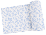 The Angel Dear Swaddle Blanket, partially unrolled and displayed, features a blue floral and bow print on white fabric—ideal for crafting a soft bamboo baby blanket.
