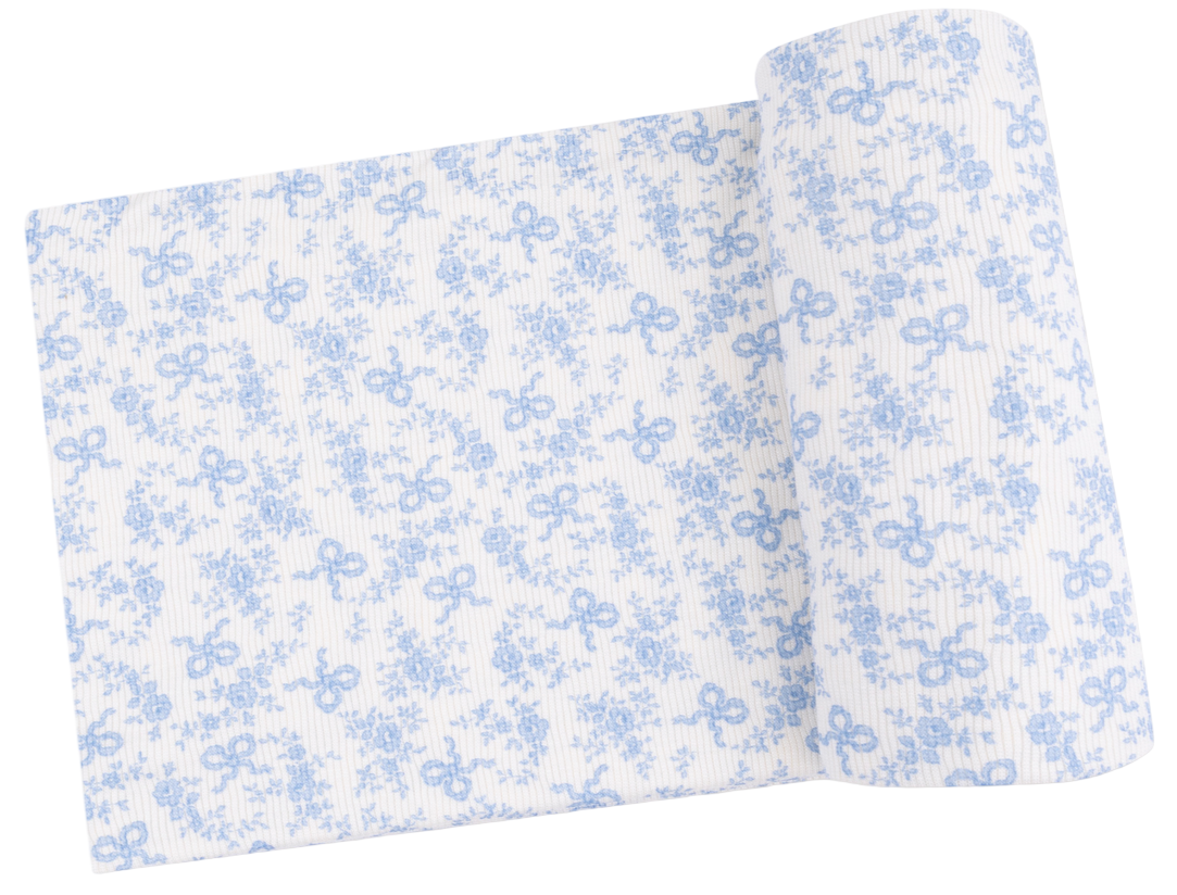 The Angel Dear Swaddle Blanket, partially unrolled and displayed, features a blue floral and bow print on white fabric—ideal for crafting a soft bamboo baby blanket.